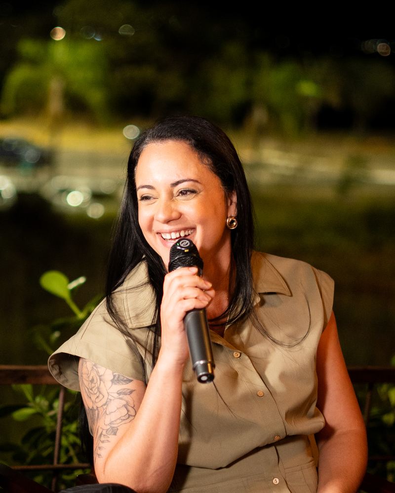 Participante com o microfone na mão se apresentando para as outras mulheres da mesa.